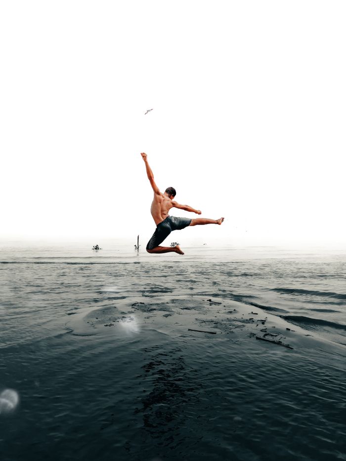 Shirtless man energetically jumping over the ocean, creating a dynamic and captivating scene.