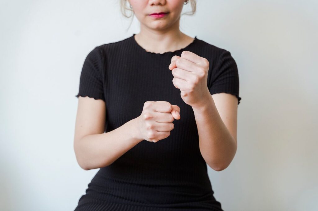 Close-up of a woman in a black shirt making fist gestures against a white background.