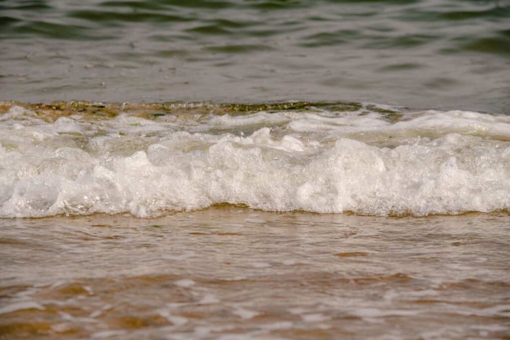 Close-up view of gentle ocean waves creating foam on a sandy beach.